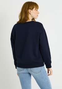 Sudadera de color azul marino con un ajuste relajado, puños y dobladillo acanalados, y cuello redondo. El material parece suave y texturizado, adecuado para un uso casual.