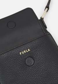 Borsa in pelle nera con texture a ciottoli, logo dorato "FURLA" e chiusura a bottone circolare. Presenta una tracolla tono su tono per il trasporto.