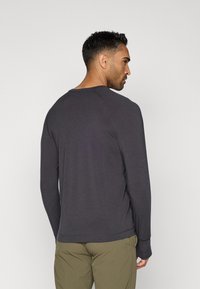 Σκούρο γκρι μακρυμάνικο μπλουζάκι από μαλακό ύφασμα, με στρογγυλή λαιμόκοψη και ράγλιν μανίκια, συνδυασμένο με ανοιχτό πράσινο παντελόνι.