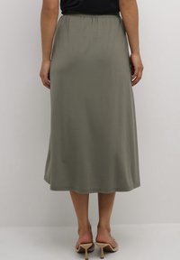 Khaki midi-rok met een elastische tailleband, een gladde textuur en een rechte snit. Gecombineerd met open schoenen.