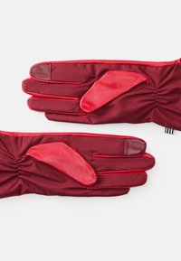 Red gloves featuring a smooth leather palm and finger accents, with a gathered fabric design. Made of stretchy material for improved fit.