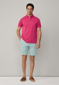 Růžové polo tričko s tříknoflíkovou léga, spojené se světle modrými šortkami a hnědými surovými lodními botami. Jednoduchý, ležérní letní outfit.