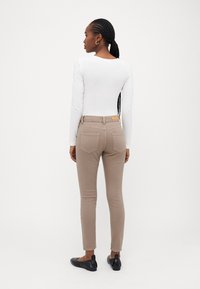 Beige bukser med tilpasset pasform og baglommer, parret med en hvid langærmet top. Materialet ser blødt ud, med en slim silhuet og ankellængde.