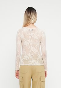 Blonder langermet topp i lys beige med blomstermønster; gjennomsiktig mesh-materiale med rund hals og tettsittende silhuett.