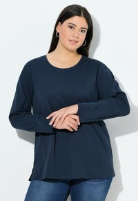 Langärmliges navy T-Shirt aus weichem Stoff mit Rundhalsausschnitt und seitlichen Schlitzen am Saum, kombiniert mit blauen Jeans. Einfaches und lässiges Design.