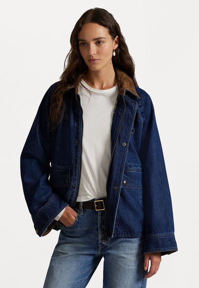 Mørkeblå denimjakke med et kordfløjlskrave, knap- og lynlåslukninger samt to forlommer. Båret over en hvid t-shirt og jeans.