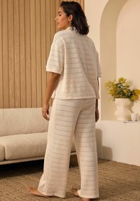Cremfarbenes Strick-Loungewear-Set mit einem T-Shirt mit kurzen Ärmeln und weit geschnittenen Hosen, beide mit vertikalen strukturierten Streifen. Weicher, lockerer Schnitt.