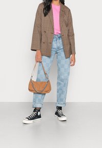 Brązowa dwurzędowa marynarka w kratę, różowa koszula, jasno niebieskie jeansy w kratę, czarne wysokie trampki oraz brązowa torba sztruksowa z łańcuszkiem.