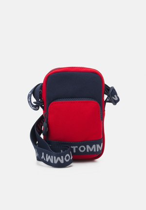 Petit sac bandoulière rectangulaire rouge et marine avec poche avant et sangle marine réglable avec texte blanc.