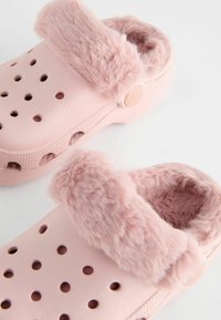 Sabots en caoutchouc rose et tout en douceur, dotés de perforations pour la ventilation, d'une doublure en fausse fourrure douce et d'une semelle texturée pour une meilleure adhérence.