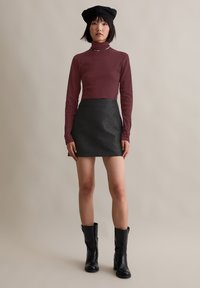 Bordeauxkleurige coltrui, gestructureerde zwarte mini-jurk, zwarte enkellaarzen en zwarte hoed. Eenvoudig ontwerp, aansluitende pasvorm, gladde stof en patroon details.