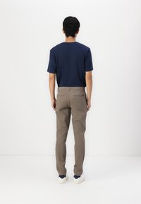 Marineblaues Kurzarm-T-Shirt kombiniert mit hellbraunen Hosen. Die Schuhe sind weiß mit einer strukturierten Sohle. Einfaches Design, keine sichtbaren Muster oder Logos.
