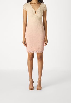 Femme portant une robe en dentelle à manches courtes avec un décolleté en trou de serrure en dégradé de beige à rose clair, associée à des talons beiges à bride cheville.