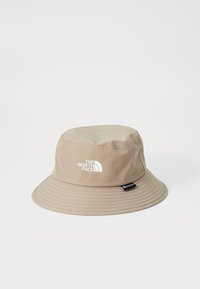 Cappello a secchiello beige realizzato in materiale impermeabile, con un logo bianco sul davanti, tesa larga e superficie testurizzata.