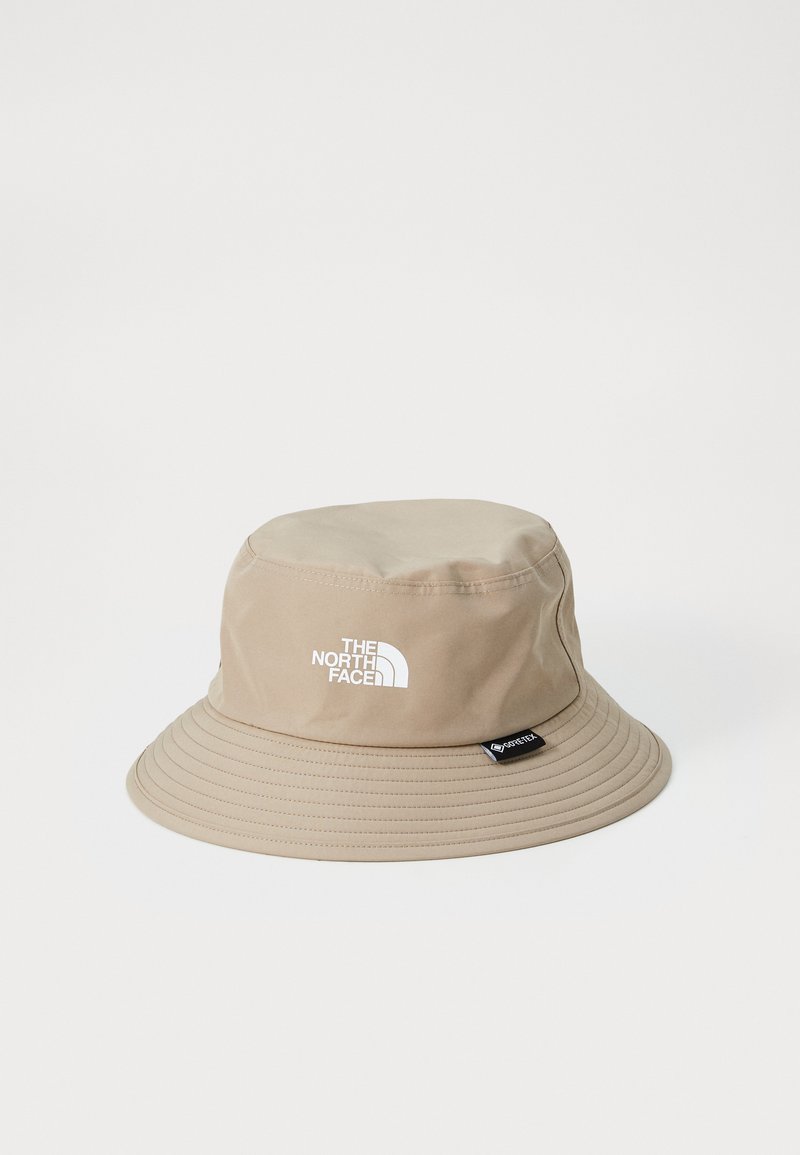 Cappello a secchiello beige realizzato in materiale impermeabile, con un logo bianco sul davanti, tesa larga e superficie testurizzata.