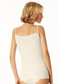Jasno beżowy top na ramiączkach z cienkimi paskami, gładką teksturą, dopasowanym krojem i prostym końcem. Widok z tyłu, w połączeniu z jasno kolorową bielizną.