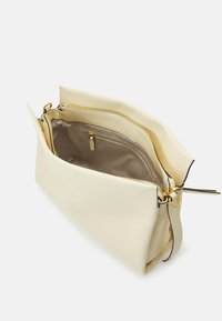 Krämfärgad läderväska med en strukturerad yta, två zippered fack och detaljer i guldmetall. Öppen design som avslöjar tygfoder.