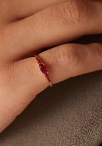 Roze gouden ring met een ovale robijn als middelpunt, omringd door kleinere robijnen, gezet op een gestructureerde achtergrond.