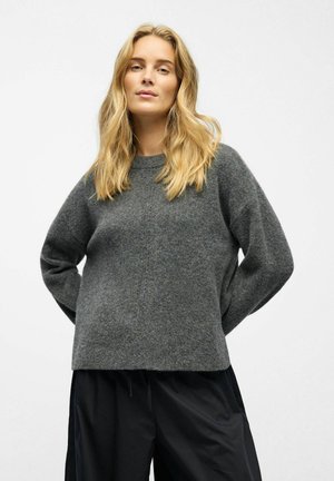 Maglione grigio in maglia testurizzata con una vestibilità rilassata, scollo a girocollo e spalle cadenti, abbinato a pantaloni neri larghi.