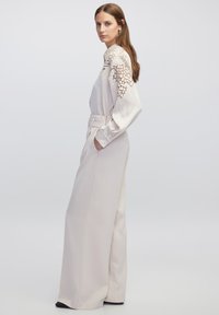 Crème jumpsuit met kantdetails op de mouwen, hoge kraag, zijzakken en een wijde pijpdesign, gemaakt van glad, gestructureerd materiaal.