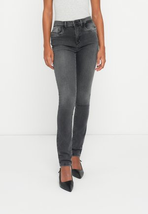 Slim fit high-waisted faded black jeans worn with black pointed-toe heels and a light gray sleeveless top on a plain background.