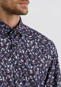 Overhemd met knopen op een marineblauwe achtergrond, versierd met een multicolore bloemenpatroon. De stof lijkt glad, met een traditionele kraag en knopen.