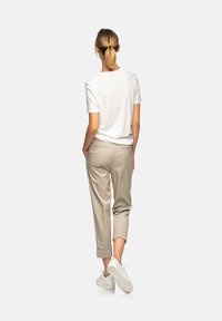 Biała bawełniana koszulka, beżowe spodnie o kroju cropped z podwiniętymi mankietami oraz białe trampki. Gładka tkanina z prostym wzorem i subtelnymi detalami szwów.