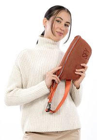 Compacte tas in roestoranje met een gestructureerde buitenkant en een zilveren rits, voorzien van een duurzame, verstelbare band. Zachte, wit geribbelde trui.