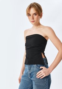 Top negro sin mangas con fruncido en la parte delantera y aberturas laterales, hecho de una tela suave. Combinado con vaqueros de tiro alto azul.