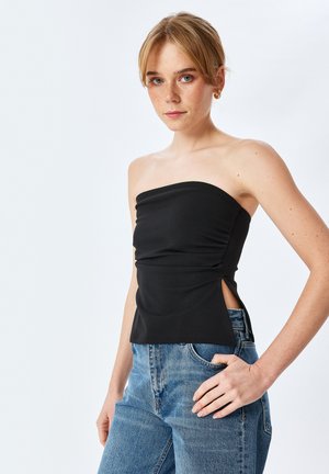 Top negro sin mangas con fruncido en la parte delantera y aberturas laterales, hecho de una tela suave. Combinado con vaqueros de tiro alto azul.