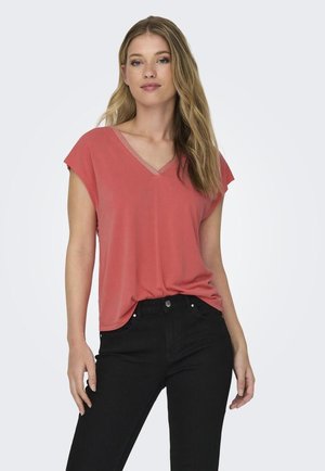 Camiseta de cuello en V color coral con mangas cortas, textura suave y detalles sutiles a lo largo del escote, combinada con jeans negros de corte ajustado.