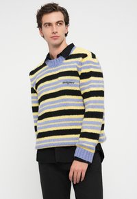Pull rayé en jaune, noir et lavande, fabriqué en maille texturée. Doté d'un col rond et du logo "tommy" sur la poitrine.