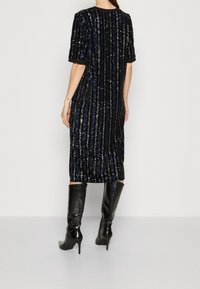 Svart paljettklänning i midilängd med vertikala ränder, korta ärmar och rund halsringning, kombinerad med knähöga svarta klackstövlar.