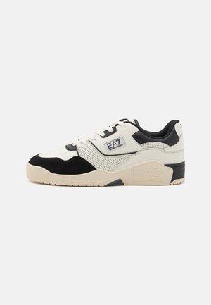 Black and white athletic shoe with perforated leather, suede accents, and a chunky sole. Features a logo patch on the side and contrasting laces.