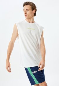 Mouwloos wit sportshirt met "KEEP MOVING FORWARD" in het groen. Gecombineerd met marineblauwe shorts met een groene zijstreep en het "GOLF" logo.