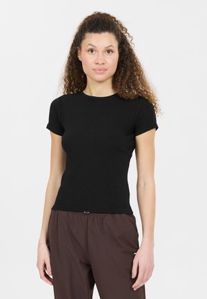 Haut court noir à côtes avec une coupe ajustée. En coton, col rond, associé à un pantalon marron ample et un accent métallique subtil.