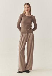Bruine, getailleerde trui met lange mouwen en geribbelde zoom, gecombineerd met lichtbeige hoge taille wijde broek. Glad textuur van de stof en subtiele glans.