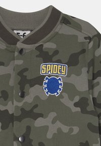 Maskáčová mikina v zelených tónech s žebrovaným límcem. Obsahuje modrou vyšitou nálepku 'SPIDEY' a ikonu pavouka, která je zapnuta černými knoflíky.