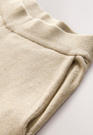 Pantaloni de trening bej cu talie elastică plisată și textură moale. Materialul pare ușor texturat, cu un finisaj neted.