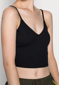 Débardeur court noir côtelé avec bretelles fines et col en V, présentant une coupe ajustée qui met en valeur une silhouette élancée.