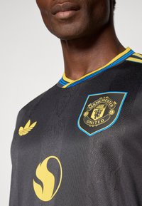 Μαύρη φανέλα της Manchester United με κίτρινες και μπλε λεπτομέρειες. Διαθέτει στρογγυλή λαιμόκοψη, κεντητό λογότυπο και υφασμάτινη υφή.