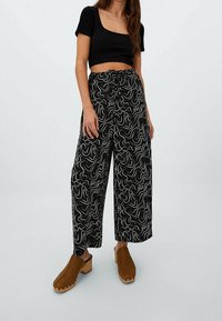 Černobílé vzorované kalhoty s širokými nohavicemi a stahováním v pase, doplněné úzkým černým crop topem a hnědými dřeváky.