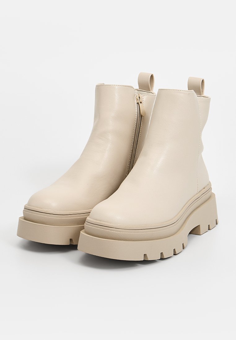 Beige Stiefel aus Kunstleder mit einer klobigen Plateausohle, seitlichem Reißverschluss und einer Zuglasche auf der Rückseite. Glatte Textur mit minimalistischem Design.
