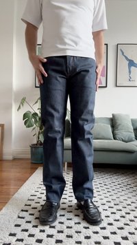 Temno modri jeans z rednim krojem, ravnim sprednjim delom in klasičnim dizajnom s petimi žepi. Oblečen z črnimi čevlji in belo srajco.