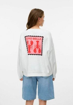 Witte sweatshirt met een roze kreeftafbeelding en de tekst "CIAO BELLA", voorzien van een geschulpte rand. Gecombineerd met blauwe denim shorts.
