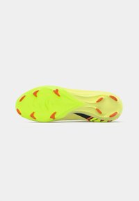 Suela de zapatilla deportiva de color amarillo brillante, con tacos de goma en acentos rojos y negros, superficie texturizada y forma aerodinámica para un mejor rendimiento.