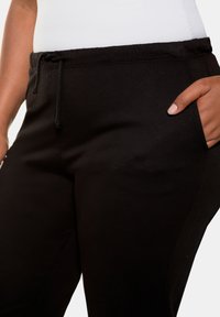 Zwarte joggers met een trekkoord in de taille, zijzakken en een gladde textuur. Gemaakt van zachte, ademende stof voor comfort.
