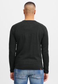 Chemise noire à manches longues avec texture côtelée, encolure ronde et manches raglan, associée à un jean bleu avec coutures sur les poches arrière.