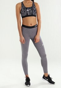 Top sportivo con un motivo astratto nero e grigio; leggings grigi abbinati con una texture sottile; entrambi presentano il logo Nike; sneakers nere.