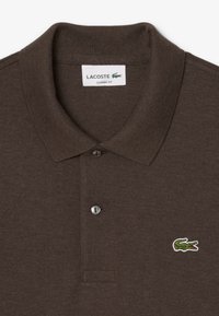 Polo marrone realizzato in tessuto texturizzato, con colletto classico, due bottoni e logo di un coccodrillo ricamato in verde sul lato sinistro del petto.